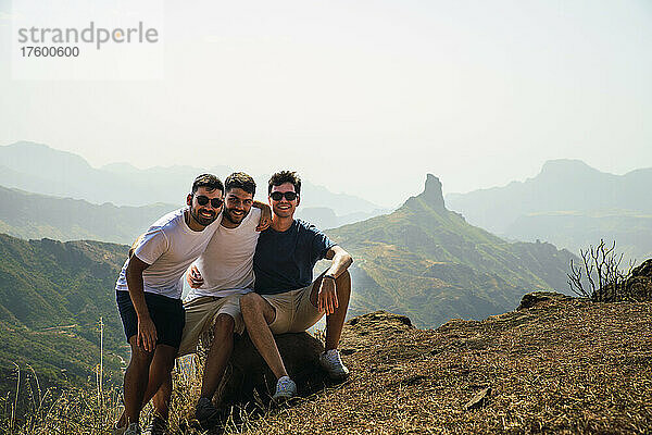 Fröhliche junge Freunde sitzen auf einem Felsen in Degollada de Becerra  Spanien