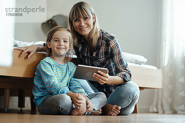 Lächelnde Frau und Sohn mit Tablet-PC im Schlafzimmer zu Hause