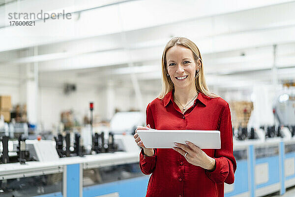 Glückliche Geschäftsfrau mit Tablet-PC in der Fabrik