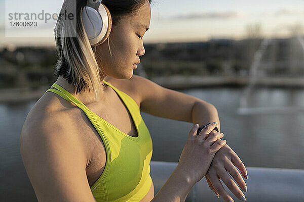 Junger Sportler mit Kopfhörern überprüft die Zeit auf der Armbanduhr
