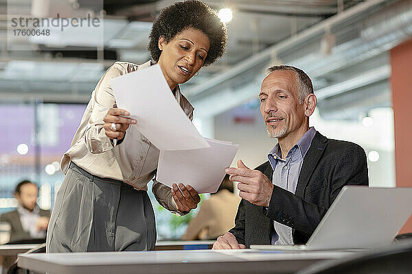 Businessman discussing with colleague over documents in coworking space