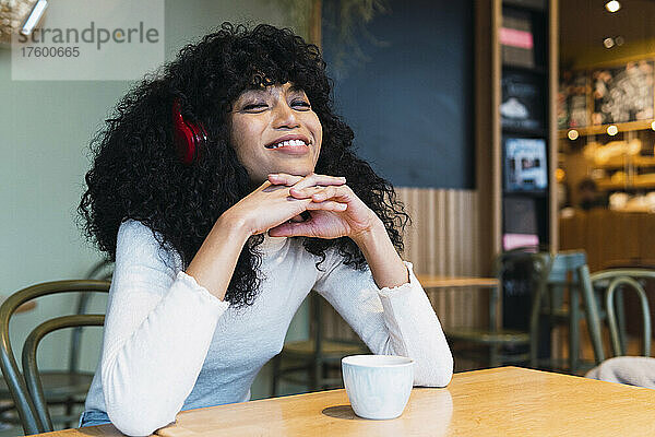 Lächelnde junge Frau mit gefalteten Händen am Kinn  die im Café Musik hört