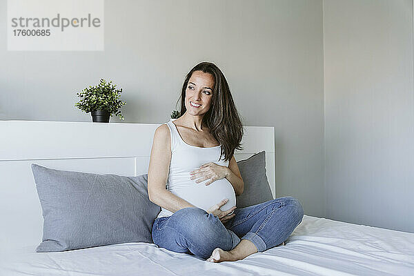 Glückliche schwangere Frau mit langen braunen Haaren  die zu Hause im Bett sitzt