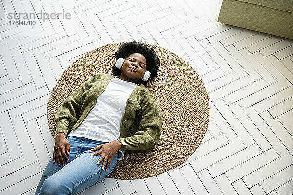 Young woman relaxing and listening music through headphones lying on floor