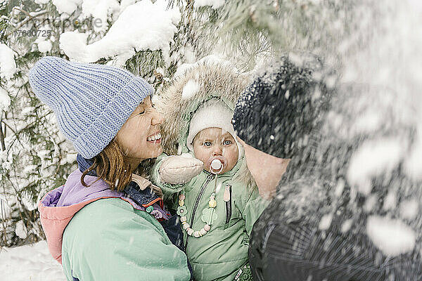 Frau trägt Tochter von Mann  der im Winter mit Schnee spielt
