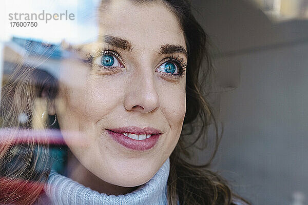 Nachdenkliche Frau mit blauen Augen  durch Glas gesehen
