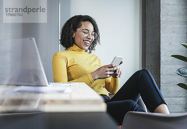Fröhliche Geschäftsfrau nutzt Smartphone im Büro