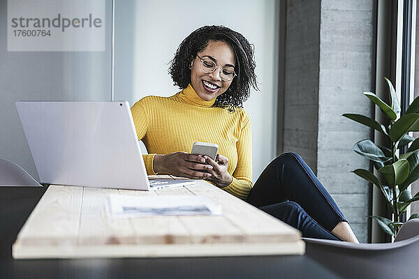 Lächelnde Geschäftsfrau  die im Büro Textnachrichten auf dem Smartphone sendet