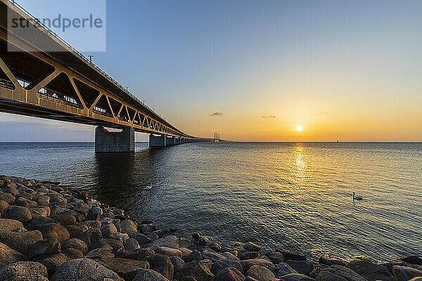 Öresundbrücke bei Sonnenuntergang mit felsigem Ufer im Vordergrund