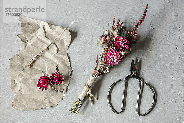 Studio shot of scissors  piece of paper and small bouquet of dried flowers