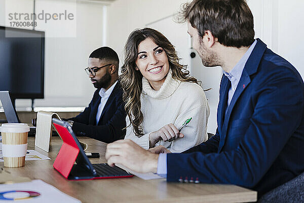 Lächelnde Geschäftsfrau diskutiert mit Kollegen im Coworking-Büro