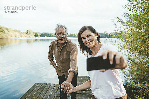 Glückliche Frau macht Selfie per Smartphone mit älterem Mann am Steg