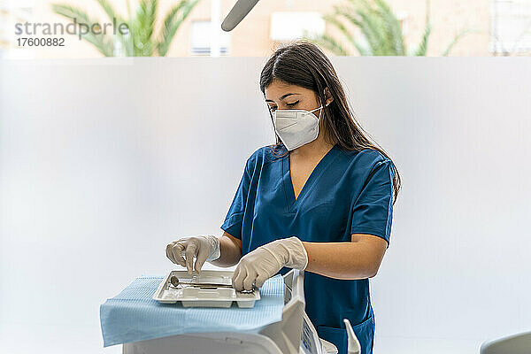 Krankenschwester trägt eine schützende Gesichtsmaske und arrangiert zahnärztliche Ausrüstung in der medizinischen Klinik