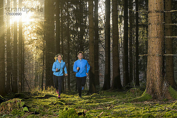 Mann und Frau joggen bei Sonnenuntergang im Wald
