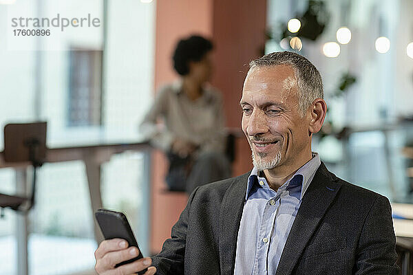 Lächelnder Geschäftsmann benutzt Smartphone im Büro