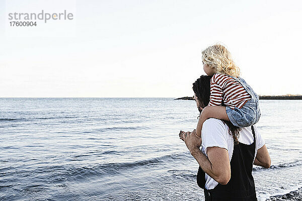 Mann trägt Sohn auf Schultern am Meeresufer am Strand