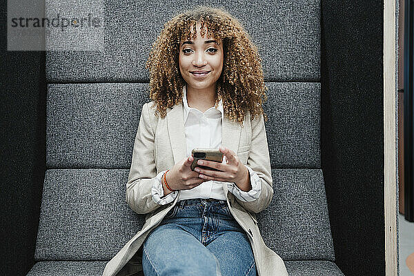 Lächelnde Geschäftsfrau mit Mobiltelefon sitzt im Büro