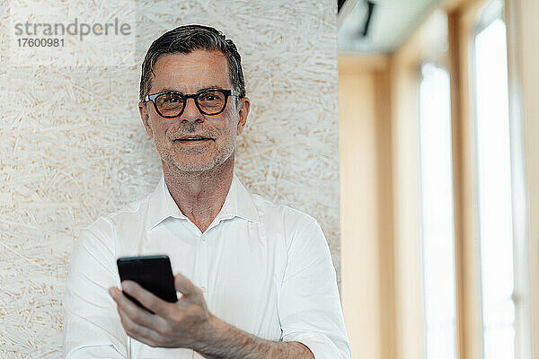 Geschäftsmann mit Brille hält Smartphone vor Wand