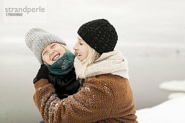 Glückliche Mutter umarmt fröhliche Tochter und genießt den Winter