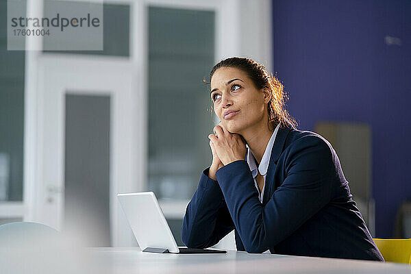 Geschäftsfrau sitzt mit Tablet-PC und träumt am Schreibtisch