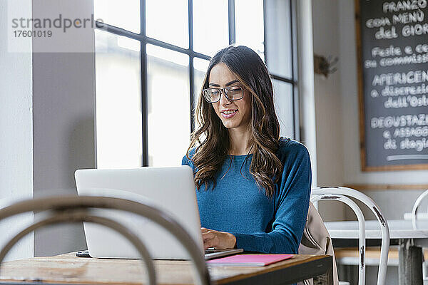 Lächelnde junge Geschäftsfrau  die im Café am Laptop arbeitet