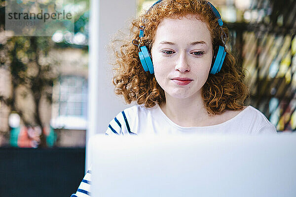 Rothaarige Frau benutzt Laptop und hört Musik über Kopfhörer im Café