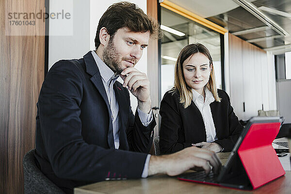 Geschäftsmann teilt Tablet-PC mit Geschäftsfrau  die am Schreibtisch im Büro sitzt
