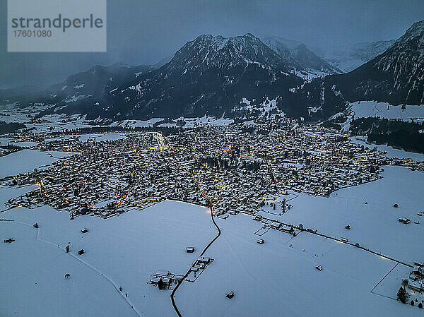Deutschland  Bayern  Oberstdorf  Hubschrauberaufnahme einer schneebedeckten Stadt in den Allgäuer Alpen in der Abenddämmerung