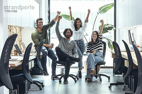 Cheerful multiracial businessmen and businesswomen with arms raised in coworking office