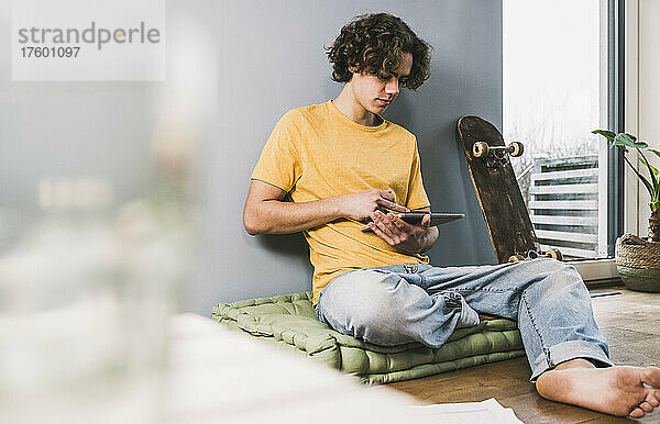 Junger Mann nutzt Tablet-PC mit Skateboard zu Hause