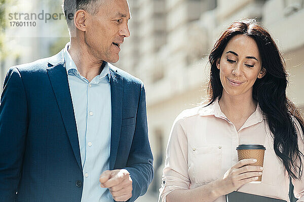 Geschäftsmann spricht mit Geschäftsfrau  die an einem sonnigen Tag eine Einwegkaffeetasse in der Hand hält