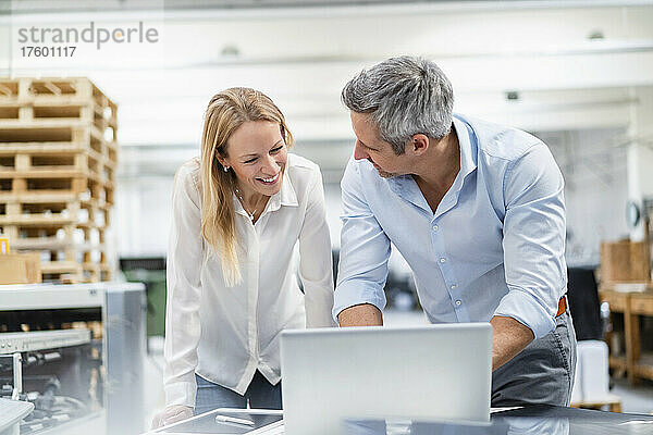 Lächelnder Geschäftsmann und Geschäftsfrau diskutieren über Laptop in der Industrie
