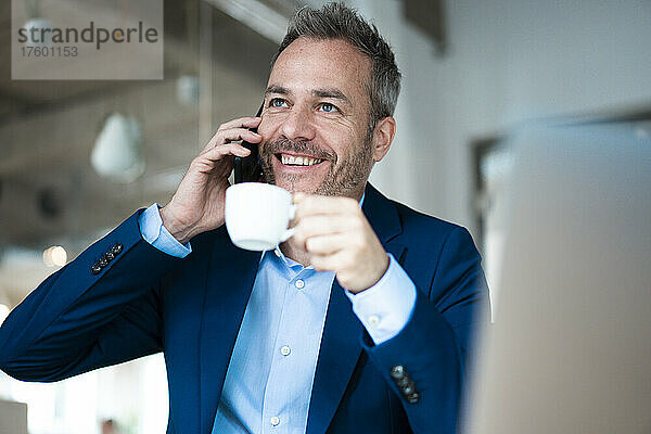 Smiling businessman holding coffee cup talking on mobile phone