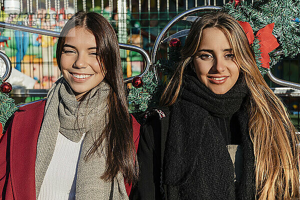 Lächelnde junge Freunde mit langen Haaren tragen an sonnigen Tagen warme Kleidung