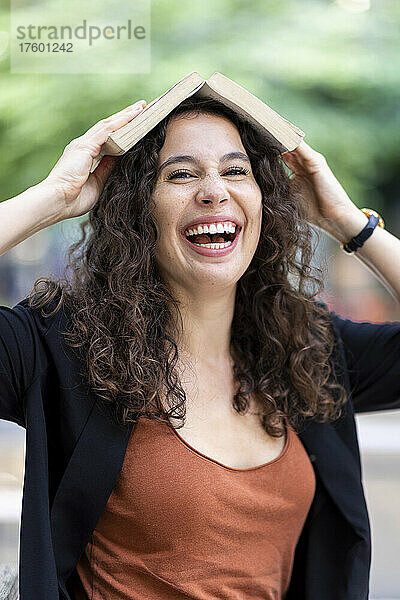 Junge Frau lacht und hält Buch auf dem Kopf