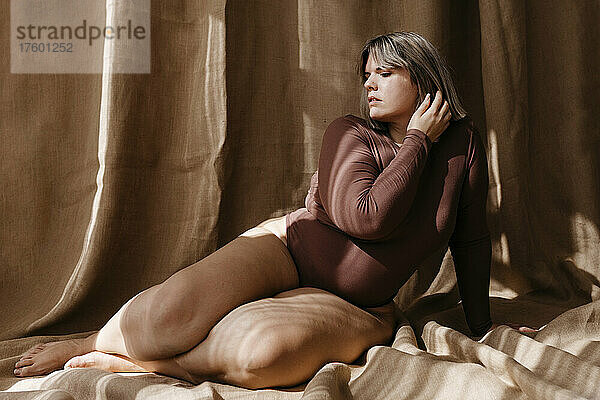 Beautiful curvy woman with hand in hair in front of brown backdrop