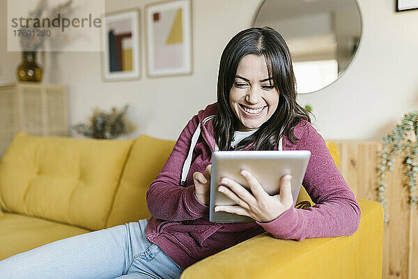 Glückliche Frau sitzt zu Hause auf dem Sofa und benutzt einen Tablet-PC