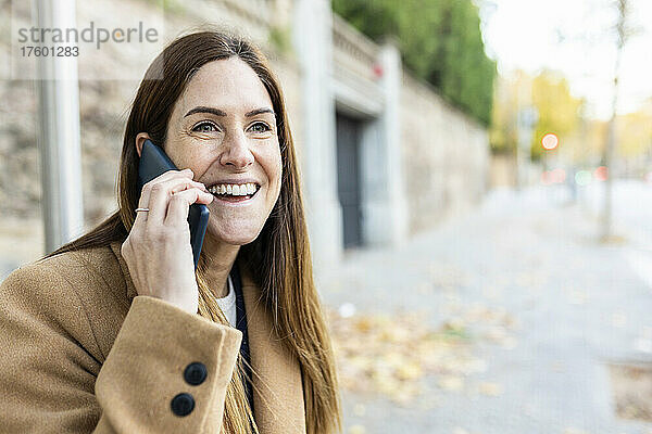 Fröhliche Frau mit braunen Haaren  die auf dem Smartphone spricht