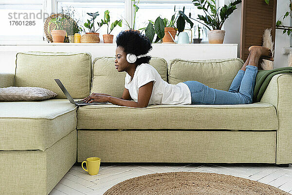 Junge Geschäftsfrau mit Kopfhörern und Laptop zu Hause auf dem Sofa