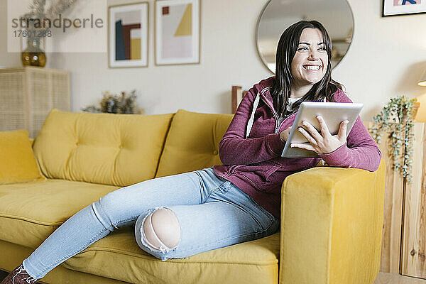 Glückliche junge Frau mit Tablet-PC sitzt auf dem Sofa im Wohnzimmer