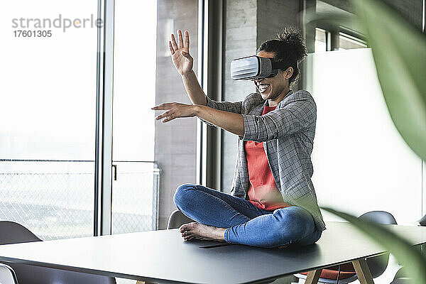 Lächelnde Geschäftsfrau mit VR-Brille gestikuliert im Büro