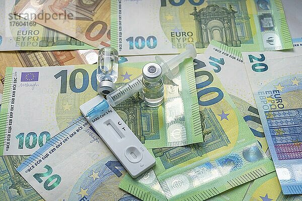 Geld (Euro-Banknoten) mit medizinischer Maske  Antigentest  Impfstoffflaschen und Spritze. Finanzkrise aufgrund von Coronavirus-Verlusten  selektiver Fokus