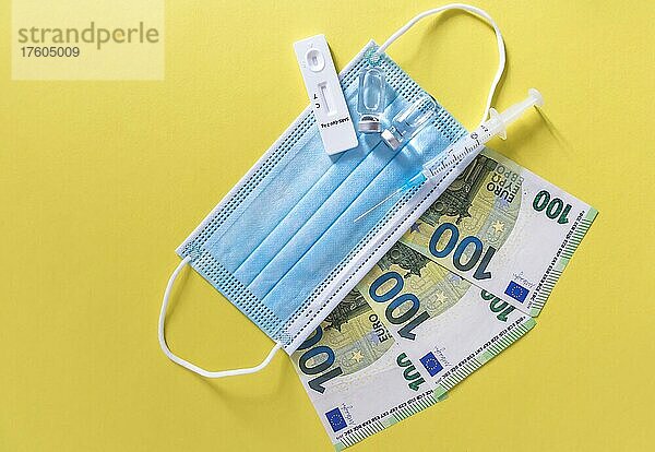 Geld (Euro-Banknoten) mit medizinischen Masken  Antigentest  Impfstoffflaschen und Spritze. Finanzkrise aufgrund von Coronavirus-Verlusten  selektiver Fokus
