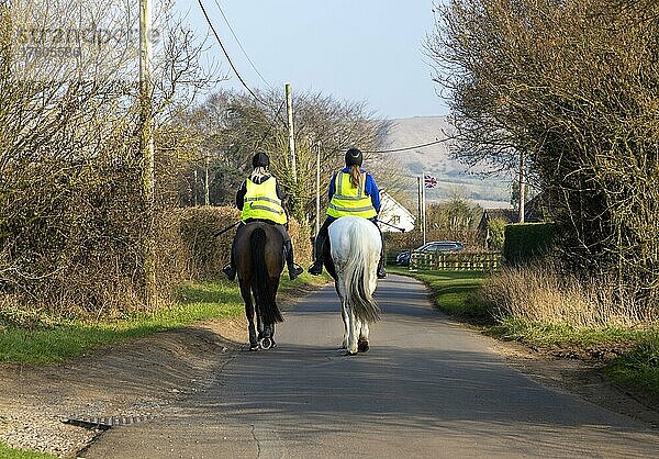 Zwei Frauen reiten auf Pferden entlang einer ruhigen Landstraße  Bromham  Wiltshire  England  UK