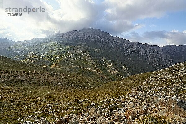 Frühling auf Kreta  Morgenlicht  Dorf Thripti an grünem Berghang  graues Gebirgsmassiv  wolkiger Himmel  Sonne scheint durch Wolken hindurch  bewachsener Hang und Geröll  Thripti-Gebirgsmassiv  Ostkreta  Insel Kreta  Griechenland  Europa