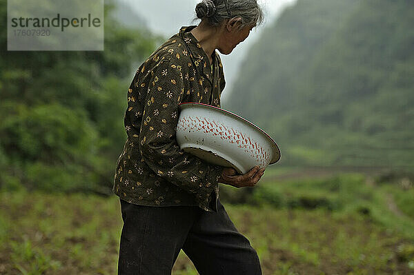 Ein Dorfbewohner sät Samen in den Boden  umgeben von einer wunderschönen Karstlandschaft; Wulong  Provinz Chongqing  China.
