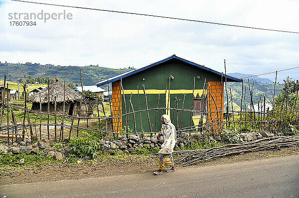 Frau geht die Straße entlang  vorbei an Häusern in einem ländlichen Dorf in Äthiopien; Äthiopien
