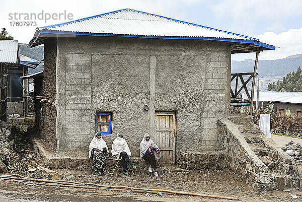 Drei Menschen sitzen vor der Tür eines Hauses im Hochland von Äthiopien; Äthiopien