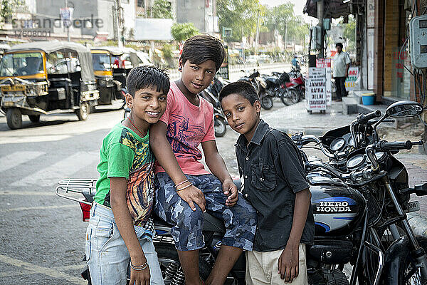 Drei Jungen versammeln sich auf einer Straße um ein Motorrad und schauen in die Kamera; Amritsar  Punjab  Indien