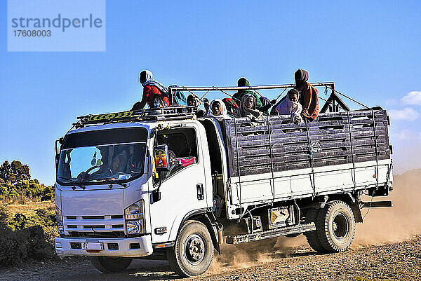 Menschen stehen auf der Ladefläche eines Lastwagens  der auf einer staubigen  unbefestigten Straße im ländlichen Äthiopien fährt; Äthiopien
